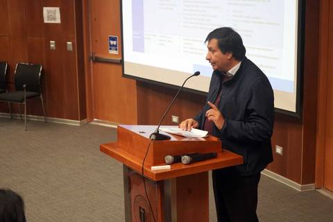 Un hombre está dando una charla en un auditorio con un proyector de fondo.