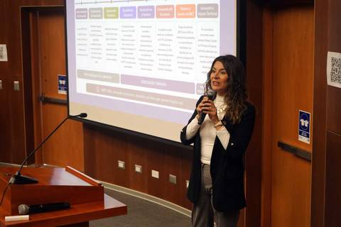 Una presentadora expone en una conferencia frente a una pantalla con gráficos y datos.