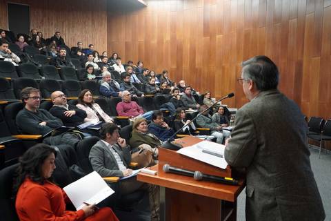 Un académico presenta un tema ante un grupo de personas en un auditorio lleno.