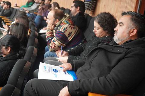 Un grupo de personas escuchando atentamente durante una presentación en una sala.
