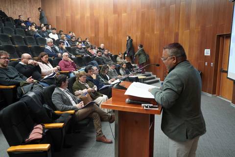 Una charla en un auditorio con un expositor y varios asistentes atentos.