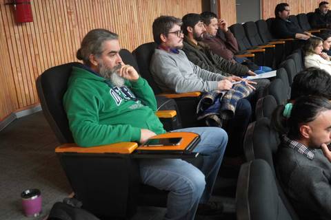 Un grupo de personas sentadas en un auditorio, algunas miran hacia adelante y otras parecen pensativas.