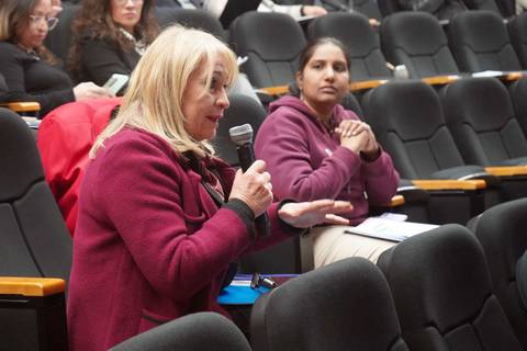 Una mujer está hablando en un evento mientras otra persona la escucha atentamente.