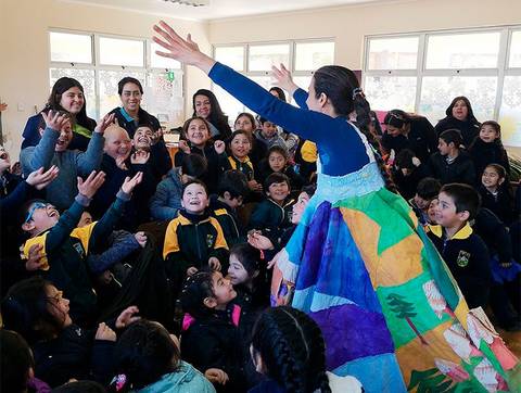 Un grupo de niños y adultos disfrutan de una presentación artística en un ambiente alegre y colorido.