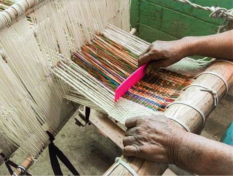 Una persona está tejiendo en un telar manual con hilos de colores.