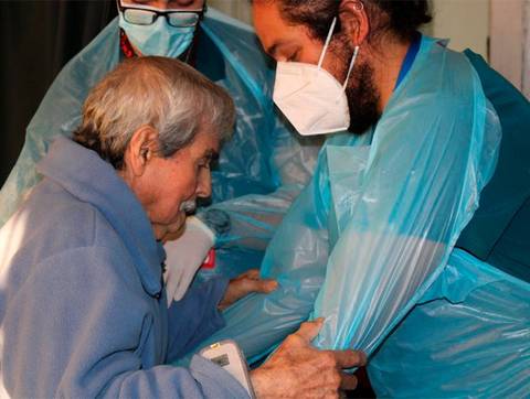 Dos personas cuidan a un anciano mientras se prepara para recibir atención médica.