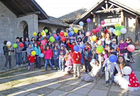 Un grupo grande de niños y adultos sonrientes sosteniendo globos de colores en un lugar al aire libre.