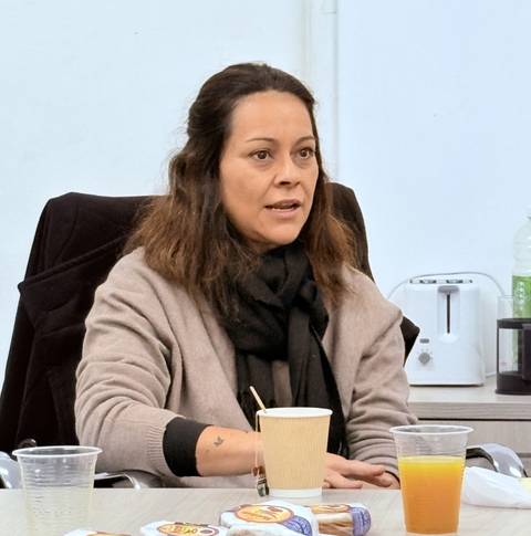 Una mujer sentada en una mesa con bebidas y snacks, luciendo interesada en la conversación.