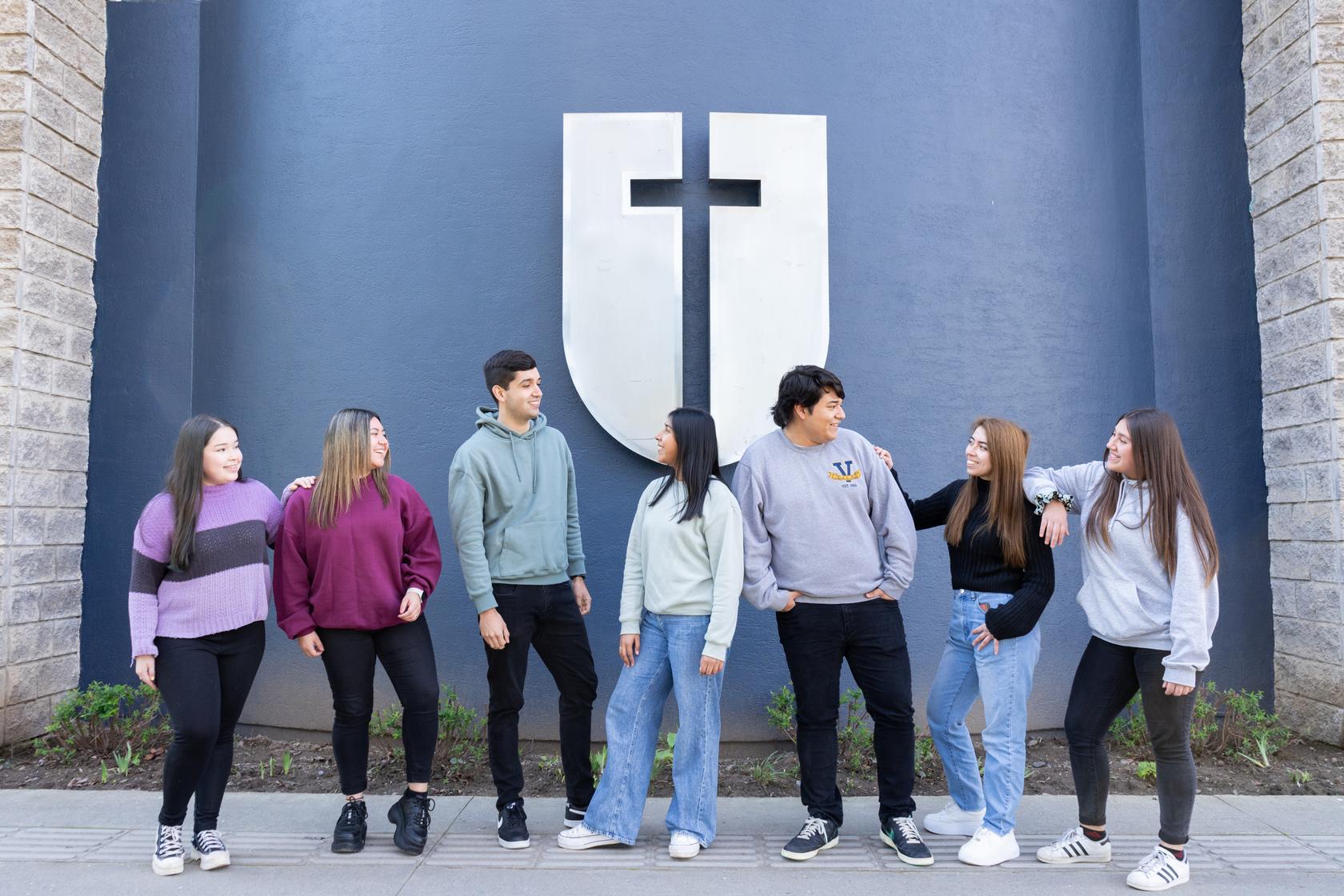 Un grupo de jóvenes conversando amigablemente frente a un mural con una cruz.