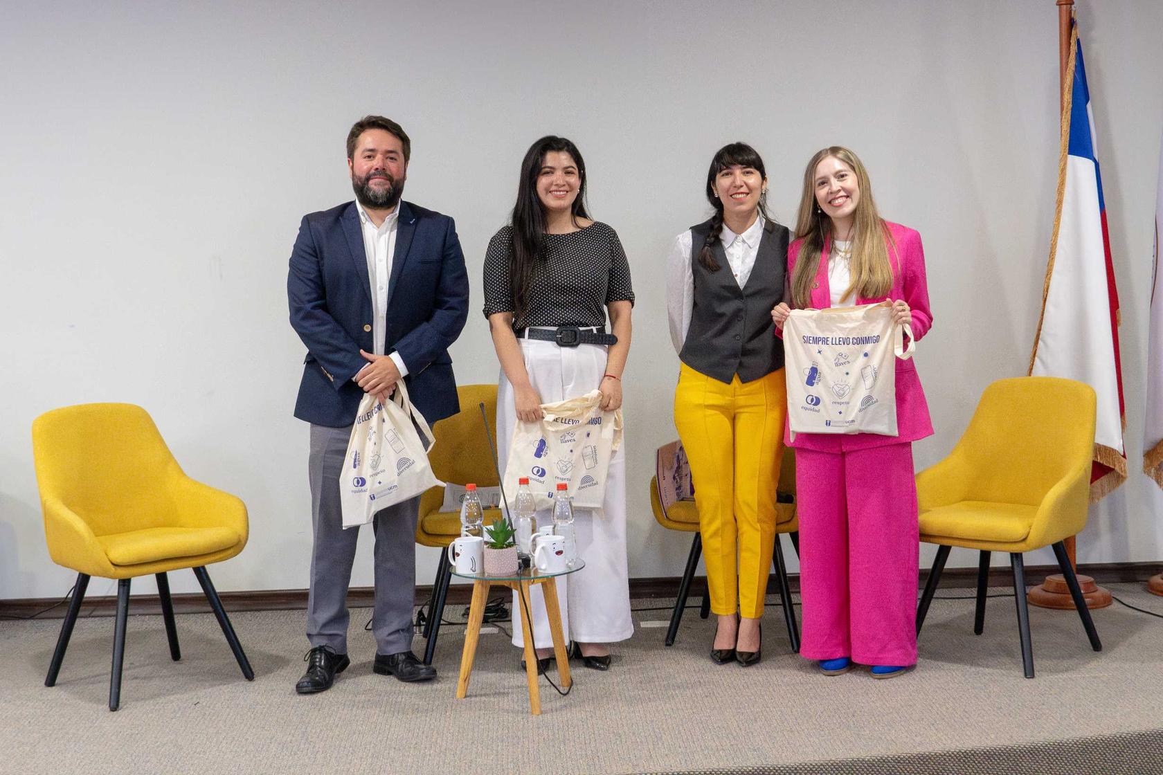 Cuatro personas posan sonrientes en un evento, sosteniendo bolsas con el logo de la actividad.