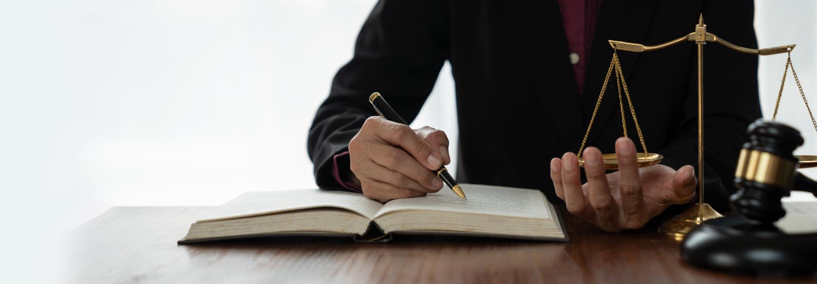 Un abogado escribiendo en un libro mientras sostiene una balanza de la justicia.