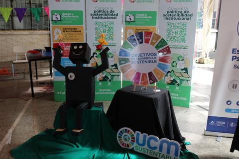 Una figura de cartón de un personaje sonriente junto a una rueda con los Objetivos de Desarrollo Sostenible en un evento de sostenibilidad.
