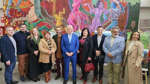 Un grupo de personas posando sonrientes frente a un mural colorido en un evento cultural.