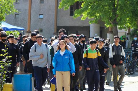 Un grupo de estudiantes caminando por un patio escolar en un día soleado.