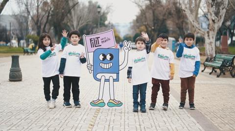 Un grupo de niños en una plaza sosteniendo un cartel con un personaje animado.