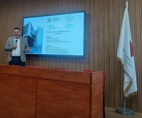 Un presentador está hablando frente a una pantalla en un auditorio.