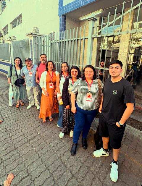 Un grupo de ocho personas sonriendo frente a una entrada con reja en un día soleado.