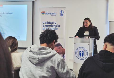 Una mujer expone en una charla frente a un grupo de personas en un salón.