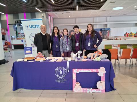 Un grupo de personas posando junto a una mesa de información en un espacio público.