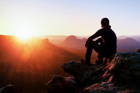 Una persona contempla el amanecer desde lo alto de una roca en un paisaje natural.