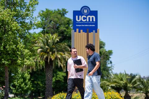 Dos estudiantes conversando en el Campus San Isidro de la UCM bajo el sol.