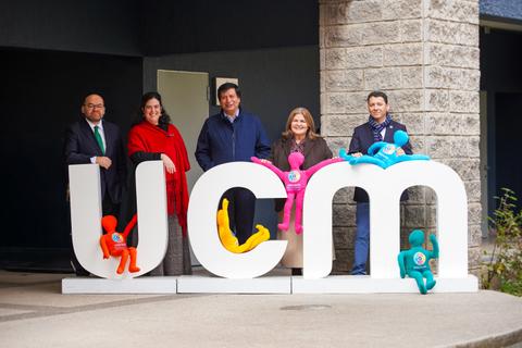 Un grupo de personas posando frente al letrero de UCM, decorado con figuras coloridas.