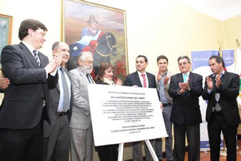 Un grupo de personas participan en un acto de inauguración en una sala con un cuadro en el fondo.