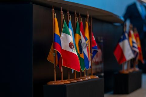 Una fila de banderas de distintos países, incluyendo Chile, Colombia y México, exhibidas en un evento.
