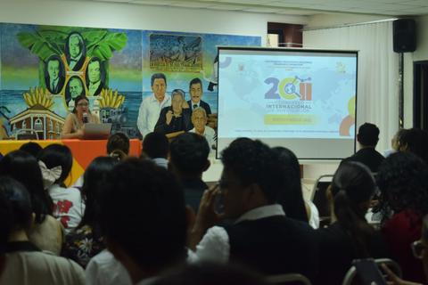 Presentación en un evento internacional con un mural colorido de fondo.