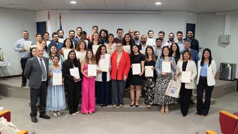 Un grupo grande de personas sonrientes sosteniendo sus certificados en un evento de premiación.