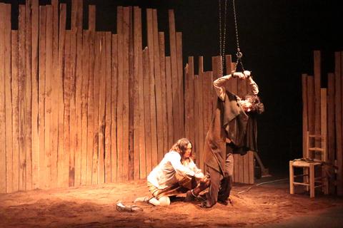 Una escena teatral que muestra a dos personajes en un ambiente rústico con paredes de madera.