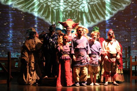 Un grupo de niños y adultos en un escenario durante una representación teatral con trajes elaborados.