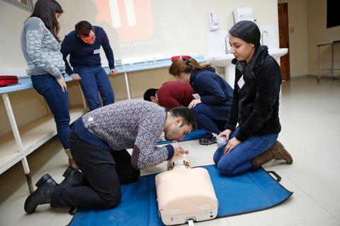 Un grupo de personas está aprendiendo técnicas de resucitación cardiopulmonar sobre un maniquí en un aula.