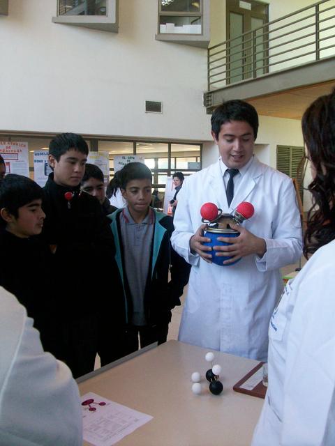 Un grupo de estudiantes observa a un docente que explica conceptos científicos utilizando un modelo de molécula.