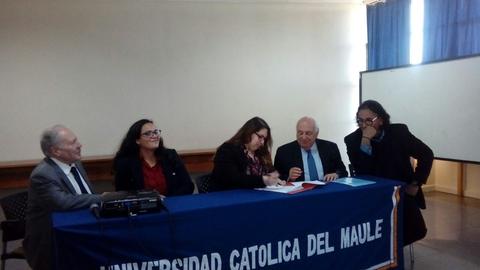 Un grupo de personas firmando un documento en una mesa en un evento de la Universidad Católica del Maule.