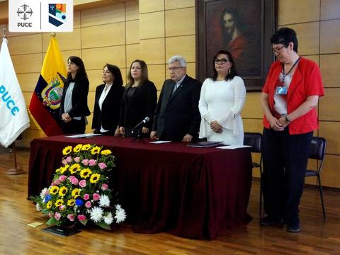 Una ceremonia formal con varias personas de pie junto a una mesa decorada con flores.