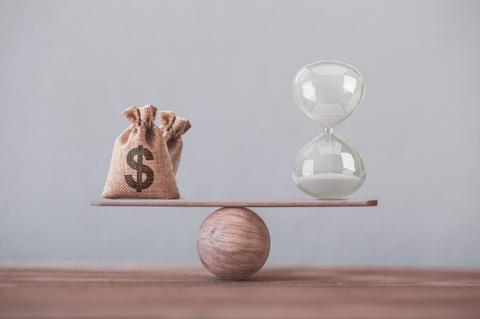 La imagen representa un equilibrio entre una bolsa de dinero y un reloj de arena.