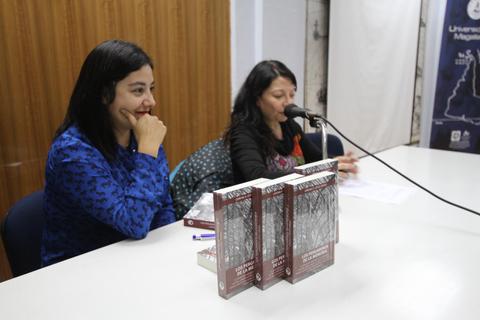 Dos mujeres participan en una actividad de presentación de libros en un ambiente académico.