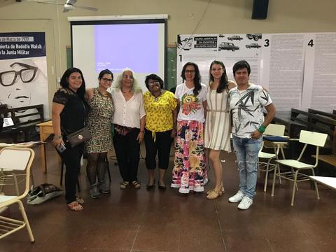 Un grupo de personas se reúne en un evento dentro de un salón con proyecciones y carteles en la pared.