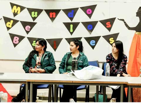 Un grupo de tres mujeres sentadas frente a una pancarta que dice 'Mundos de Baile'.