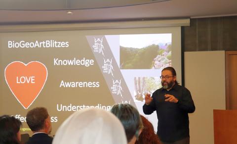 Una persona hablando en una presentación mientras se proyectan imágenes relacionadas con el medio ambiente en la pantalla.