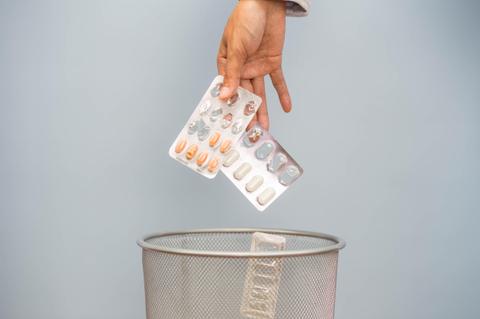 Una mano tira un paquete de medicamentos a un cubo de basura.