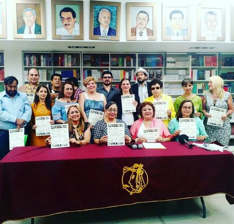 Un grupo de personas posando con certificados en un evento formal en una biblioteca.