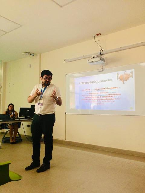 Un hombre presenta información en una sala de clases frente a una pantalla con un tema sobre antecedentes generales.