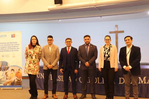 Un grupo de seis personas posando frente a un cartel y una cruz en un evento en la Universidad Católica de Maule.