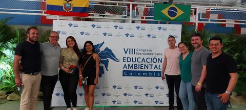 Un grupo de personas posando frente a un fondo con el logo del VIII Congreso Iberoamericano de Educación Ambiental en Colombia.