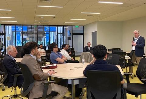 Una reunión en un espacio moderno donde un orador se dirige a un grupo de personas sentadas en torno a una mesa.