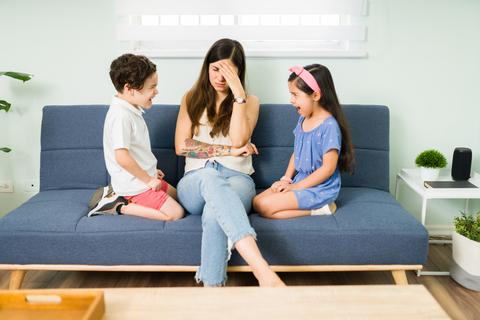Una madre se siente abrumada mientras sus dos hijos conversan animadamente a su lado.
