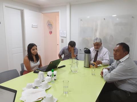 Reunión de trabajo en una sala con varias personas sentadas alrededor de una mesa.