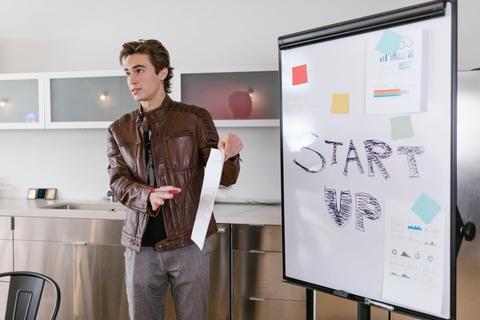 Un joven presenta una idea en una sala de reuniones con una pizarra que dice 'START UP'.
